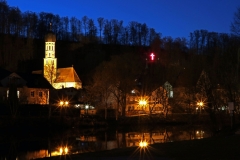 Wolfratshausener Altstadt mit beleuchtetem Kreuz im Bergwald von Hubert Blockinger